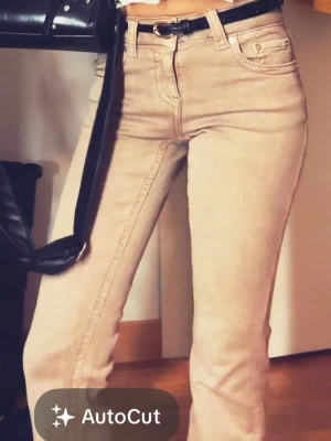 Beige raka jeans med fickdetaljer - Snygga beige jeans med raka ben och klassisk femficksmodell. Jeansen har dekorativa ficklock med knapp bak och bälteshällor i midjan. Perfekta för en trendig och avslappnad look.