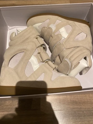 Isabel marant skor - Säljer ett par snygga höga sneakers från Isabel Marant i beige mocka och vitt läder. Skorna är helt oanvända dock så har lådan en liten defekt i det vänstra hörnet. Tveka inte på att höra av dig vid minsta lilla fundering