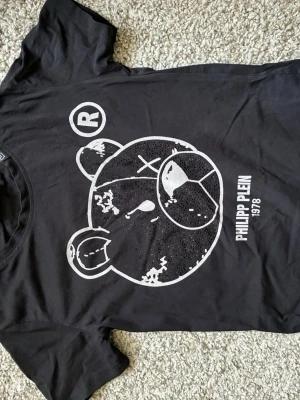 Svart Philipp Plein t-shirt med björn - Cool svart t-shirt från Philipp Plein med stort vitt tryck av en björn på framsidan och texten 'PHILIPP PLEIN 1978'. På ryggen finns en exklusiv logodetalj i metall. T-shirten har rund hals och är tillverkad i mjuk bomull.