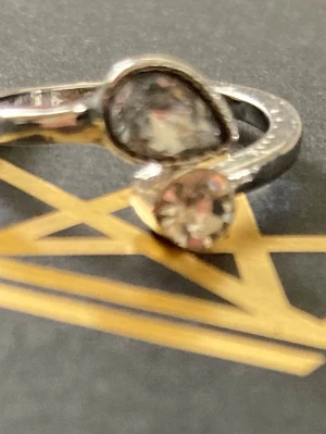 Silverring med två stenar - Snygg silverfärgad ring med två stenar, en rund och en droppformad. Ringen har en öppen design där stenarna möts framtill och ger ett modernt intryck. Perfekt för dig som gillar unika detaljer och stilrena accessoarer.