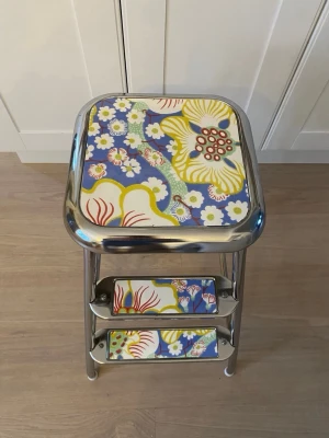 Beslag/klädsel till Awab/Lindkvist kökspall/stegpall Svenskt Tenn Eldblomman - Beslag/klädsel till Awab/Lindkvist  Färdigklippt klädsel till stegpall. Motiv Svenskt Tenn ”Eldblomman”. Avtorkningsbar laminerad tålig yta.  Utklippta med sax som sedan limmas fast med kontaktlim eller dubbelhäftande tejp på stegpallen.  Obs! Pallen på bilden ingår ej utan används endast för att visa hur beslagen ska användas.  Vid köp ange i samband med betalning om du har en AWAB eller Lindkvist pall.Beslag/klädsel till Awab/Lindkvist  Färdigklippt klädsel till stegpall. Motiv Svenskt Tenn ”E