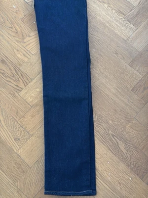 Mörkblå raka jeans från Levi's - Säljer ett par mörkblå jeans från Levi's med klassisk rak passform. Jeansen har kontrastsömmar, fem fickor och den ikoniska röda Levi's-lappen på bakfickan. Tillverkade i slitstark denim som passar perfekt till en avslappnad stil.