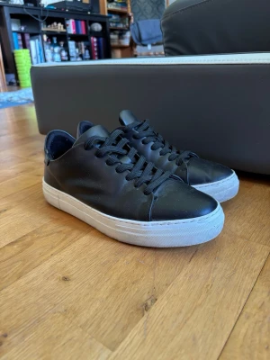 Svarta sneakers med vit sula - Stilrena svarta sneakers med slät ovandel i läderimitation och klassiska svarta skosnören. Skorna har en tjock vit sula som ger en modern look och passar perfekt till streetwear eller casual outfits. Endast använda 1 gång under min bal. Tyvärr så blev det en liten reva som man kan se på sista bilden. Inget som syns när man har på sig dem.