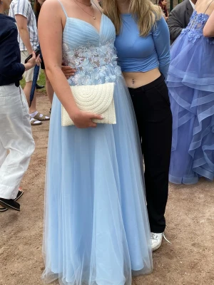 Ljusblå balklänning med spetsdetaljer - Säljer en ljusblå långklänning med tunna axelband, v-ringning och vacker spets upptill. Kjolen är i flera lager tunn tyll som ger ett drömmigt intryck. Klänningen har öppen rygg med snörning och blommigt på midjan, det är smått glitter över klänningen. Perfekt för bal till student/universitet! Nypris var 1940kr, köpare står för frakten vet inte varför det står frifrakt 