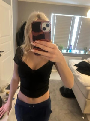 Svart croppad topp med v-ringning - Snygg svart croppad topp med v-ringning och korta ärmar. Toppen har en figurnära passform och är perfekt för att styla med både jeans och kjol. Materialet känns mjukt och stretchigt, vilket gör den bekväm att bära.