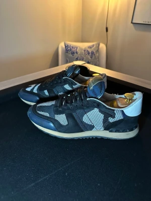 Valentino rockrunners  - Säljer ett par mycket fina Valentino Rockrunners i den klassiska camouflage-looken (blå/svart/grå). Skorna är väl omhändertagna och har alltid förvarats med skoblock för att hålla formen (skoblocken på bild ingår ej/ingår). • Modell: Rockrunner Camo • Skick: Mycket gott begagnat skick, sparsamt använda. • Äkthet: Garanterat äkta. Se bild på serienummer/produktionskod (LS U 723 Y 2) på plösen. Tyvärr finns ej kvitto eller box kvar, därav det förmånliga priset.               Storlek:43