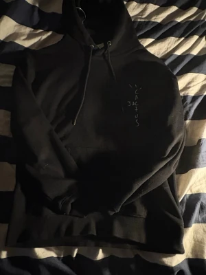  Svart tröja ifrån cactus Jack - Säljer en svart hoodie från Cactus Jack med tryck på bröstet och stor grafisk print på ryggen. Hoodien har huva med dragsko och en klassisk magficka. Perfekt för dig som gillar streetwear och vill sticka ut med en unik design.