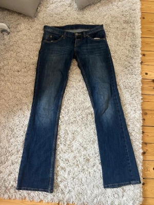 Mörkblå bootcut jeans från Wrangler - Säljer ett par mörkblå bootcut jeans från Wrangler med klassiska kontrastsömmar och broderade bakfickor. Jeansen har en lätt tvättad look och fem fickor. Perfekta för en avslappnad och snygg stil.