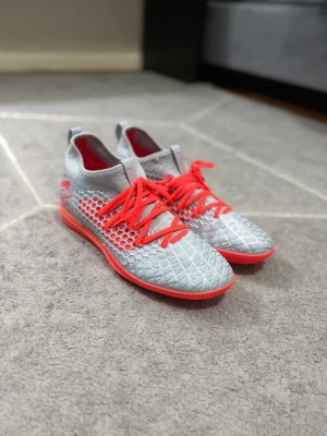 Gråa Puma fotbollsskor med röd sula - Säljer ett par gråa Puma fotbollsskor med stickad ovandel och cool struktur. Skorna har röda detaljer, röda snören och en röd sula som ger grymt grepp på planen. Perfekta för dig som vill sticka ut och ha bra kontroll på bollen.