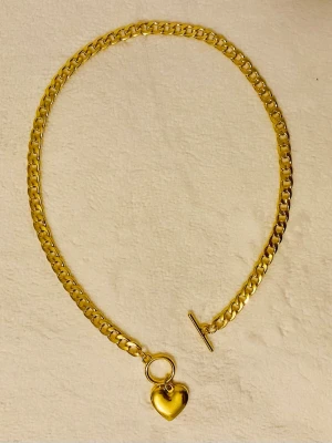 Guldigt halsband med hjärthänge - Snyggt halsband i guldfärgad rostfritt sty med en chunky kedja och ett hjärtformat hänge. Halsbandet har en dekorativ toggle-låsning framtill som ger en trendig touch. Perfekt accessoar för att lyfta din outfit med lite extra bling.