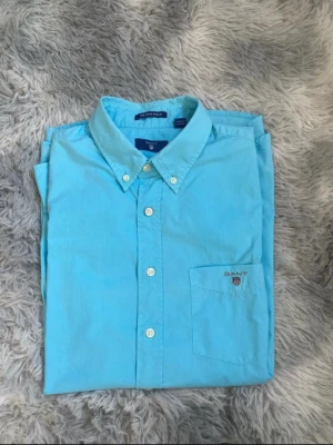 Ljusblå skjorta från Gant - Klassisk ljusblå skjorta från Gant med button-down krage och vita knappar. Skjortan har en bröstficka med Gant-logga broderad ovanför. Tillverkad i mjuk bomull och har lång ärm. Perfekt för en clean och stilren look.Den är i storlek 158/164 priset kan diskuteras vid snabb affär.