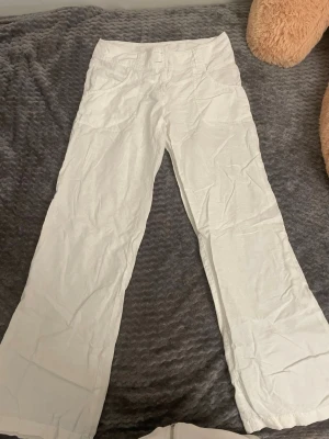 Vintage vita linnebyxor från H&M - Säljer ett par vita linnebyxor från H&M med raka ben och normal midja. Byxorna har fickor fram och stängs med knapp och dragkedja. Perfekta för en avslappnad och stilren look. Materialet är lätt och luftigt linne.