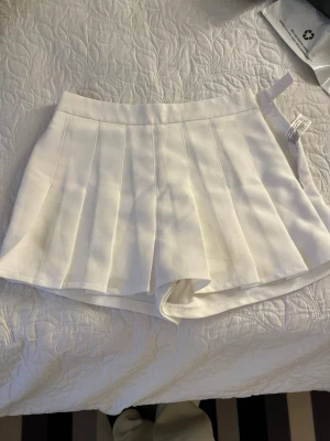 Vita plisserade skorts - Snygga vita skorts med plisserad kjol-look och inbyggda shorts. Perfekt för en sportig och trendig stil. Gjorda i ett mjukt och stretchigt material som ger en bekväm passform. Hög midja och klassisk design som passar till många outfits.