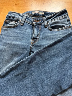 Blå Levi's jeans med raka ben - Klassiska blå jeans från Levi's med raka ben och fem fickor. Jeansen har tydliga kontrastsömmar, knappgylf och den ikoniska läderlappen bak i midjan. Tillverkade i slitstark denim som passar perfekt till en avslappnad stil.