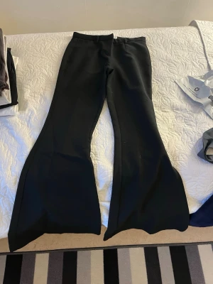 Svarta bootcut byxor med utsvängda ben - Säljer ett par svarta kostymbyxor med riktigt utsvängda ben och bootcut-modell. Byxorna har låg midja och är sydda i ett stretchigt material som ger en snygg siluett. Perfekta för dig som vill sticka ut med en trendig look.
