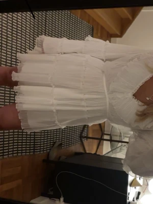 Studentklänning med volanger - Supersöt vit kortklänning från Gina Tricot med omlottmodell och volangdetaljer. Klänningen har långärmade ärmar, v-ringning och är gjord i ett lätt, plisserat tyg som ger en luftig känsla. Perfekt för studenten, använd endast en gång på min student