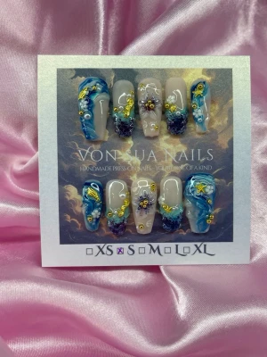 SeaJewel (S);Medium Ballerina - Unika handgjorda press-on naglar i blått och gult med 3D-nailart, pärlor och handgjorda 3Dblommor. Designen har en mix av nudebas och blå bas med detaljer i lila och guld. Perfekt för dig som vill sticka ut med kreativa och färgstarka naglar.S: 15 mm, 11,5 mm, 12 mm, 11 mm, 9 mm 