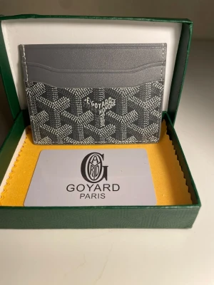 Grå kortfodral från Go4yard - Snyggt grått kortfodral från Go4yard med klassiskt mönster och logga framtill. Tillverkat i canvas och läder, perfekt för kort och ID. Kommer i originalask med tygduk och Go4yard-kort. Stilren och exklusiv accessoar för dig som gillar lyxiga detaljer.