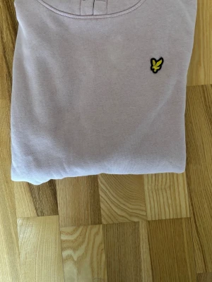 Ljusrosa hoodie från Lyle & Scott - Säljer en ljuslila hoodie från Lyle & Scott med klassisk gul logga på bröstet. Hoodien har huva och magficka, samt ribbade muddar vid ärmslut och nederkant. Perfekt för en avslappnad och stilren look. Barn ungdoms tröja 12-13 år!