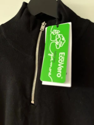 Svart stickad tröja med halv dragkedja från Lindbergh - Svart stickad tröja från Lindbergh med halv dragkedja framtill och hög krage. Tröjan har långa ärmar och ribbade muddar vid ärmslut och nederkant. Tillverkad i ett mjukt och hållbart material som känns skönt mot huden.