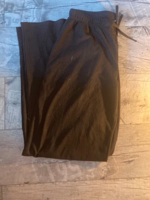 Svarta vida leggings med dragsko - Säljer ett par svarta leggings med breda ben och resår i midjan samt dragsko för justerbar passform. Materialet ser ut att vara mjukt och stretchigt, perfekt för en avslappnad look. Inga synliga fickor eller detaljer.