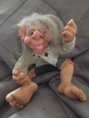 Trollfigur med glasögon och vitt hår - Säljer en rolig trollfigur med långt vitt hår, stora öron och glasögon. Figuren har en vit tröja med svarta detaljer och svarta byxor. Tillverkad i hårdplast med detaljerat ansikte och stora fötter. Perfekt som dekoration eller samlarobjekt.