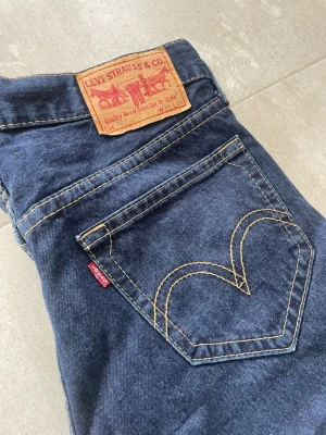 Levi's blå raka jeans - Klassiska blå jeans från Levi's med raka ben och kontrastsömmar. Jeansen har fem fickor, ikonisk läderpatch bak och den röda Levi's-taggen på bakfickan. Tillverkade i slitstark denim, perfekt för en avslappnad och tidlös stil.
