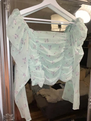 Ljusgrön blommig omlottopp - Supersöt ljusgrön topp med små blommor och draperad front. Toppen har långa ärmar och omlottdetaljer som ger en romantisk vibe. Perfekt för dig som gillar feminina och trendiga plagg.