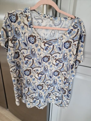 T-shirt med blått mönster. Från Soyaconcept  - Snygg t-shirt med  mönster i blått och brunt på vit botten. T-shirten har korta ärmar och en avslappnad passform med rund halsringning. Lappen är borta. Storlek XLeller XXL.