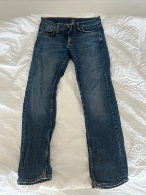 Blå jeans från Nudie Jeans - Säljer ett par klassiska blå jeans från Nudie Jeans. Jeansen har kontrastsömmar samt Nudie-logga på bakfickan. Perfekta för en stilren look. Storleken är 30/30