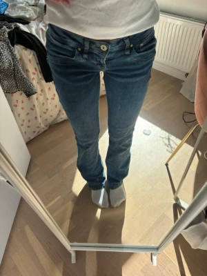 Blå bootcut jeans med låg midja - Snygga blå bootcut jeans med låg midja och klassiska fem fickor. Jeansen har en tvättad look och kontrastsömmar. Perfekta för dig som gillar en avslappnad men trendig stil.