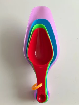 Färgglada måttskedar i plast - Ett set med fyra stapelbara måttskedar i plast i färgerna rosa, blå, grön och röd. Perfekt för bakning och matlagning, alla skedar sitter ihop med en orange ring. Skedarna har olika storlekar och tydliga måttangivelser på handtagen.