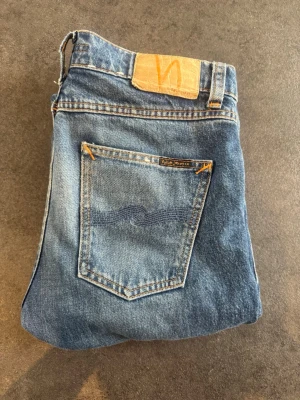 Blå jeans från Nudie Jeans - Säljer ett par klassiska blå jeans från Nudie Jeans i modellen Lean Dean. Självklart äkta! Använda då och då, men har helt klart mycket liv kvar. En liten defekt - sömmarna har gått upp lite på ett ställe, men inget som syns om du inte kollar noggrant. Storlek 29 / 30. Säljer då de blivit för små. Bara fråga vid minsta lilla!☺️