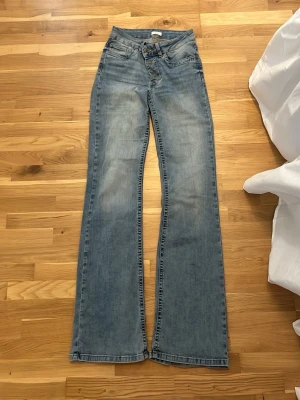 Bootcut jeans från Nelly, ljusblå - Säljer ett par ljusblå bootcut jeans från Nelly med hög midja och knappgylf. Jeansen har klassisk femficksdesign och är tillverkade i denim med lätt tvättad look. Perfekta för dig som gillar en avslappnad men trendig stil.