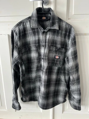 Svartvit rutig overshirt  skjorta från Dickies - Säljer en svartvit rutig overshirt skjorta från Dickies med klassisk krage och knappstängning framtill. Skjortan har en bröstficka med Dickies-logga och är långärmad. 