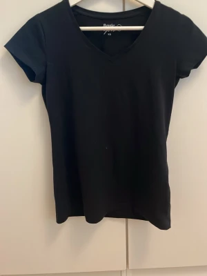 Svart v-ringad t-shirt Basic You XS - En svart t-shirt från Basic You i ekologisk bomull. Modellen har v-ringning och korta ärmar, perfekt för en clean och enkel stil. Passformen är normal och materialet känns mjukt mot huden.