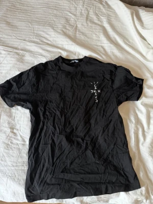 Cactus Jack t-shirt Travis Scott - Svart t-shirt från Cactus Jack med tryck fram och stort grafiskt tryck på ryggen med texten 'LOOK MOM I CAN FLY'. T-shirten har korta ärmar och normal passform. Materialet är bomull och trycken ger en streetwear vibe. Pris kan diskuteras vid snabb affär.