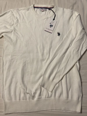 Vit tröja från U.S. Polo Assn. - Klassisk vit tröja från U.S. Polo Assn. med rund halsringning och broderad logga på bröstet. Tröjan har ribbade muddar vid ärmslut och nederkant. Tillverkad i mjukt material och har en stilren look som passar till det mesta. Helt oanvänd. Pris kan diskuteras!