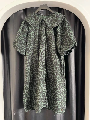 Grön leopardmönstrad klänning - Cool grön klänning med svart leopardmönster och stor krage. Klänningen har puffiga korta ärmar och en lös passform som ger en avslappnad vibe. Perfekt för dig som vill sticka ut med ett djurmönster och trendig siluett.