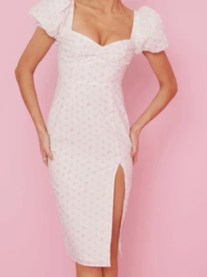 Vit blommig klänning med puffärm -  Vit klänning med små rosa blommor, puffärmar och v-ringad urringning. Klänningen har en smickrande passform och en hög slits framtill.