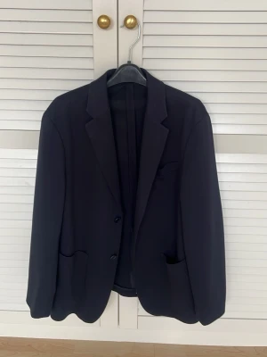 Mörkblå klassisk kavaj - Stilren mörkblå kavaj från UNIQLO med två knappar framtill, klassiska slag och tre fickor. Passar perfekt till en dressad look och har en tidlös design. 