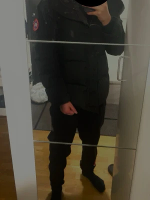 Svart dunjacka från Canada Goose - Säljer en svart dunjacka från Canada Goose med klassisk patch på ärmen och huva. Jackan har en stilren design med knappar och dragkedja framtill. Perfekt för kalla vinterdagar och riktigt varm tack vare dunfyllningen. Jag säljer den så snabbt möjligt 
