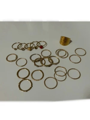 24 st Guldiga ringar - Säljer ett set med flera tunna ringar i guldfärg, vissa med infattade stenar i olika färger och en med en pärldetalj. Några ringar har tvinnad eller räfflad design, medan andra är släta. Perfekt för att mixa och matcha för en personlig stil. Säljs då de är tyvärr förstora för mig. Gissar stt storleken är L.
