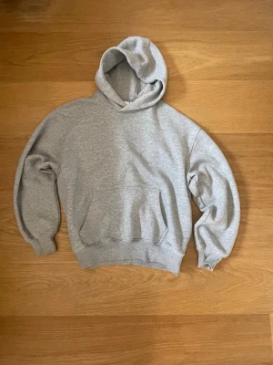 Baggy grå hoodie - En enkel och stilren grå hoodie med huva och magficka. Hoodien har ribbade muddar vid ärmslut och nederkant. Perfekt för en avslappnad look och passar till det mesta. Tillverkad i mjukt bomullsmaterial för extra komfort. Brukar ha st S-M och denna är i xs men fortfarande stor