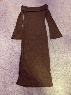 Brun ribbad långklänning offshoulder - Snygg brun långklänning med ribbad struktur och offshoulder-design. Klänningen har långa ärmar med lätt utsvängd form och omlottdetalj framtill. Perfekt för dig som vill ha en stilren och trendig look.