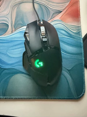 Logitech G502 HERO gamingmus - Säljer en svart Logitech G502 HERO gamingmus med RGB-belysning och flera programmerbara knappar. Musen har en ergonomisk form, metallrullhjul och kabelanslutning. Perfekt för gaming och har Logitechs ikoniska G-logga som lyser upp.