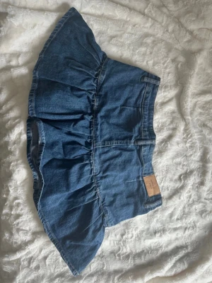 Blå volangkjol i denim från Gina Tricot  - Supersnygg blå jeanskjol från Gina Tricot med volangkant och klassiska fickor. Kjolen har en knapp och dragkedja framtill. Perfekt för dig som gillar en trendig och avslappnad stil inför våren och sommaren, eller varför inte året runt? Hör av dig kring frågor eller intressen! Kram