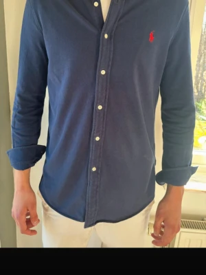 Marinblå skjorta från Ralph Lauren - Säljer denna as feta Ralph Lauren skjortan då den tyvärr ej passar. Skjortan är i väldigt bra skick. Modellen e 190. Pris 649kr, pris kan alltid diskuteras. Hör av er vid frågor eller funderingar.