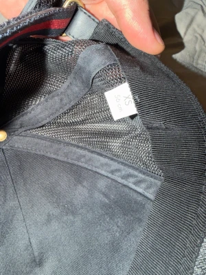 Svart keps från Gucci med GG-mönster - Snygg svart keps från Gucci i storlek XS (55 cm) med klassiskt GG-mönster på skärmen. Kepsen har mesh på insidan för extra ventilation och justerbart band med röd och grön detalj. Perfekt accessoar för en trendig streetwear-look.