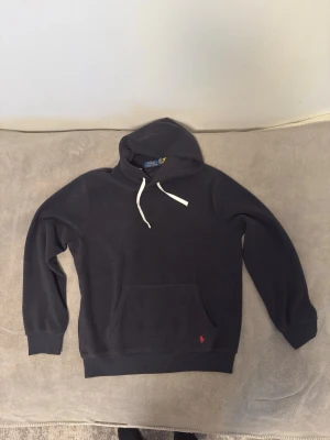 Polo Ralph Lauren fleece hoodie - Snygg svart hoodie från Polo Ralph Lauren med klassisk huva och vita dragsnören. Har en stor magficka och den ikoniska röda loggan broderad vid fickan. Tillverkad i mjukt fleecematerial som känns riktigt skönt mot huden. Perfekt för en chill och avslappnad stil.